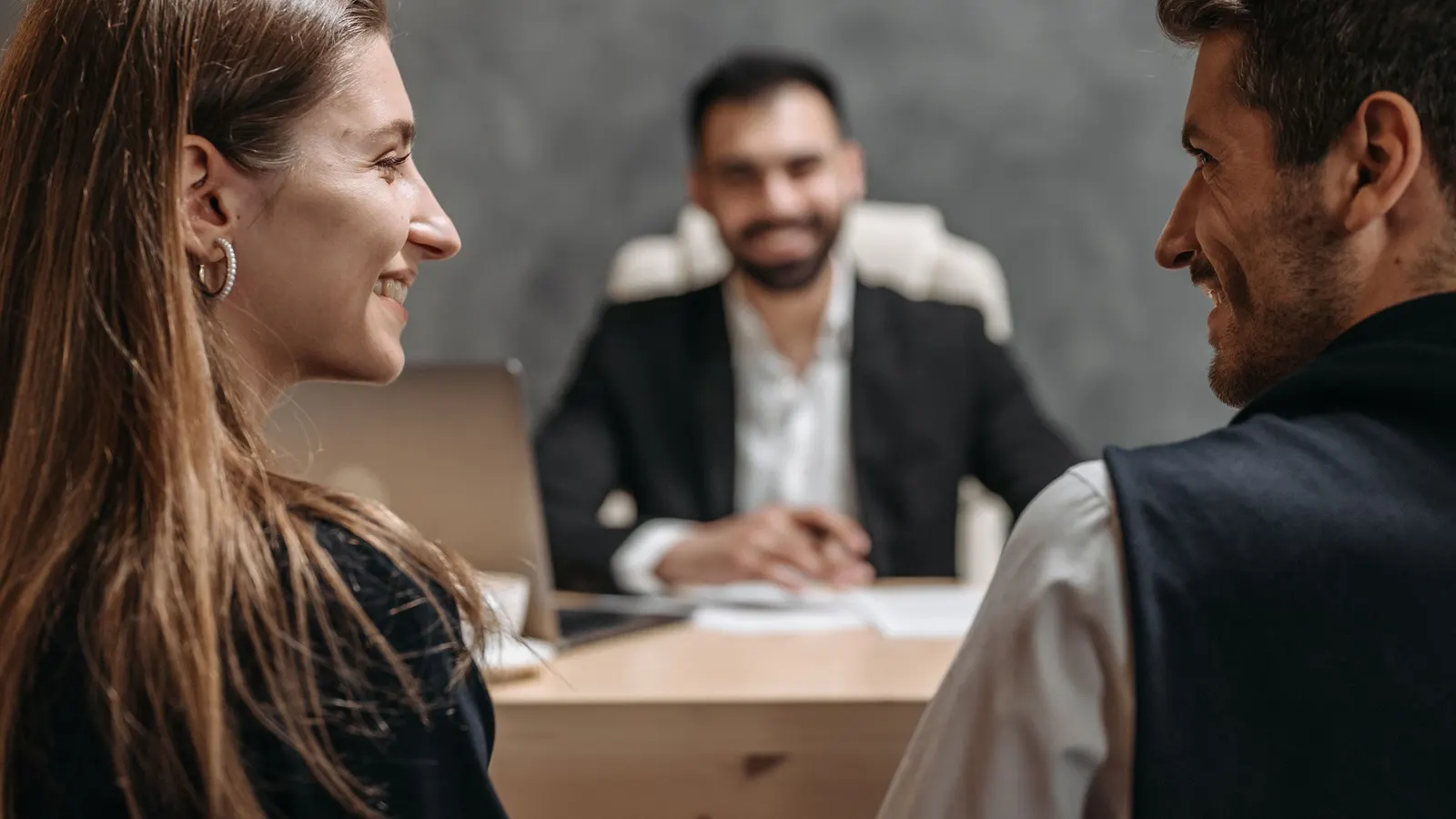 An adviser meeting two clients across a desk in a bright office.