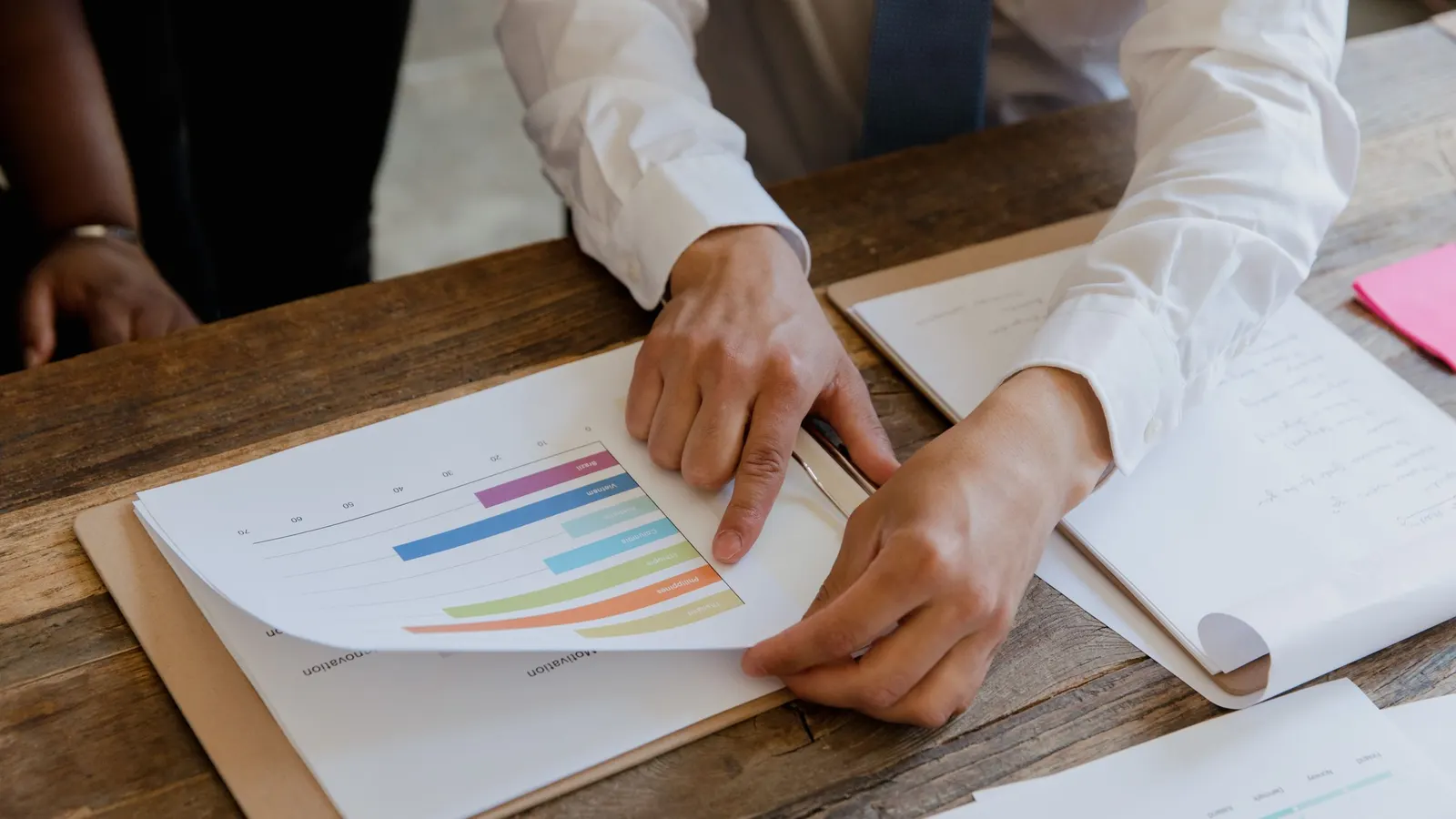 Two people reviewing a printed bar chart at a desk.
