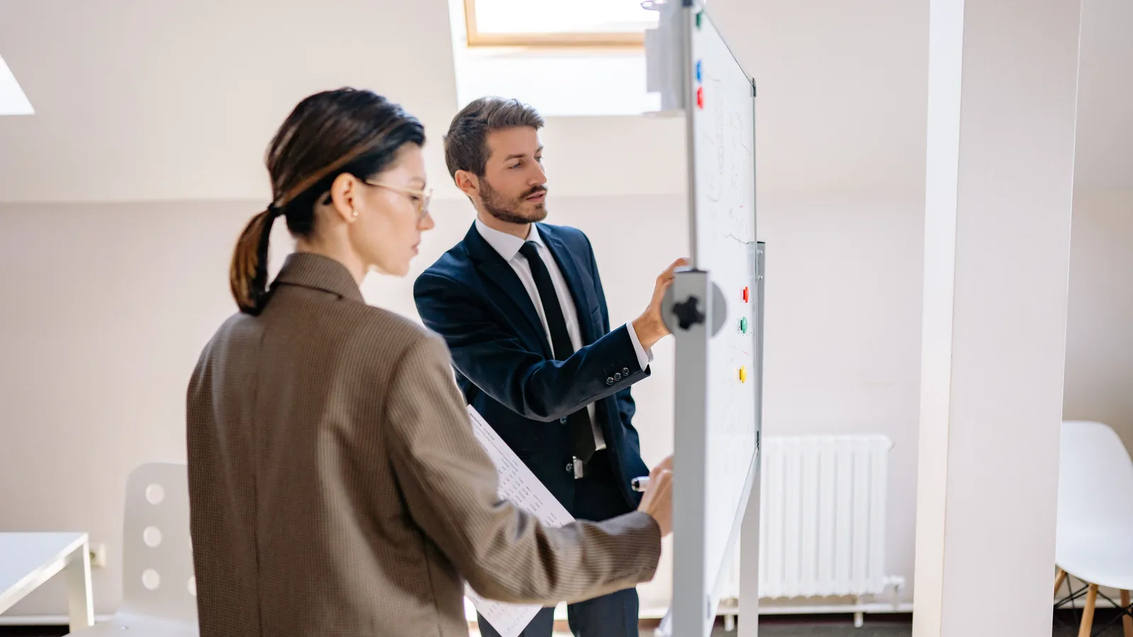 Two colleagues planning a project at a whiteboard in a bright office.