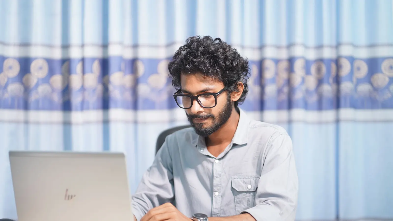 A man working on a laptop at a desk in a bright room.